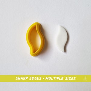 Op de afbeelding: Een gele, plastic bladvormige koekjesuitsteker naast een witte, bladvormige koek. De tekst "SHARP EDGES - MULTIPLE SIZES" is afgedrukt op een gele banner onder de afbeelding.