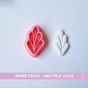 Könnte beinhalten: Zwei Ausstecher aus Kunststoff in Form eines stilisierten Blattes. Der Ausstecher links ist rosa und der Ausstecher rechts ist weiß. Der Text "SHARP EDGES - MULTIPLE SIZES" ist auf einem rosa Banner unter den Ausstechern gedruckt.