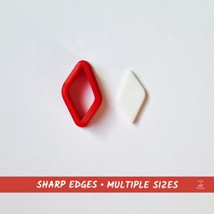 Puede incluir: Dos cortadores de galletas en forma de diamante, uno rojo y otro blanco. El cortador rojo es más grande y tiene un borde ligeramente elevado. El cortador blanco es más pequeño y tiene una superficie lisa.  "SHARP EDGES - MULTIPLE SIZES" está impreso en blanco sobre un fondo rojo.
