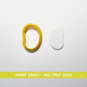 Puede incluir: Un cortador de galletas de plástico amarillo con forma de frijol, junto a una pieza de arcilla blanca con forma de frijol. El texto "SHARP EDGES • MULTIPLE SIZES" está impreso en una pancarta amarilla debajo de la imagen.
