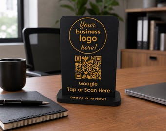 May include: A black vertical rectangular sign with a rounded top, featuring gold text that reads Your business logo here!, a gold QR code, and the text Google Tap or Scan Here and Leave a review! The sign is mounted on a black base.