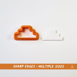 Puede incluir: Cortador de galletas de plástico naranja en forma de nube con un diseño escalonado. Se muestra un cortador de galletas de plástico blanco en forma de nube junto a él.