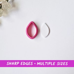 Könnte beinhalten: Ein rosa, plastikförmiger Ausstecher in Form eines Blattes und ein weißes Fondantblatt. Der Ausstecher hat scharfe Kanten. "SHARP EDGES - MULTIPLE SIZES" ist auf einem rosa Banner gedruckt.