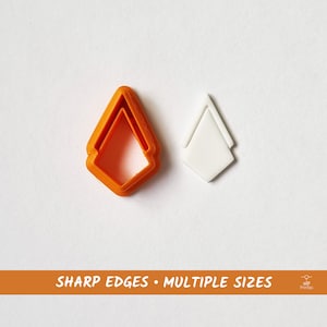 May include: Two diamond-shaped cookie cutters, one orange and one white. The orange cutter is layered, creating a multi-sized effect.  "SHARP EDGES - MULTIPLE SIZES" is printed on a banner below the cutters.