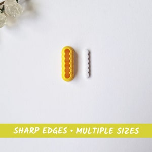 Puede incluir: Dos organizadores de cables de plástico amarillo con compartimentos de diferentes tamaños. Los organizadores están diseñados para mantener los cables y los cables ordenados. El texto "SHARP EDGES • MULTIPLE SIZES" está impreso en una pancarta amarilla en la parte inferior de la imagen.