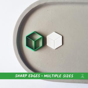 Könnte beinhalten: Zwei 3D-gedruckte Keksausstecher in Form eines Würfels, einer grün und einer weiß, auf einer grauen, strukturierten Oberfläche. Der Text "SHARP EDGES - MULTIPLE SIZES" ist unter den Ausstechern gedruckt.