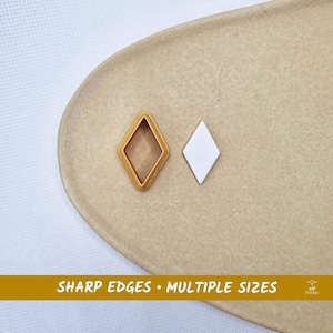 May include: Two diamond-shaped objects. One is a gold-colored outline, and the other is a solid white diamond. The objects are on a beige surface. Text at the bottom reads "SHARP EDGES • MULTIPLE SIZES".