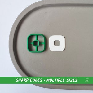 Può includere: Due stampini per biscotti quadrati, uno verde e uno bianco, su una superficie grigia. Lo stampino verde ha un quadrato più piccolo tagliato al centro e quattro linee che si estendono dal centro ai bordi. Lo stampino bianco ha un cerchio più piccolo tagliato al centro. Il testo "SHARP EDGES • MULTIPLE SIZES" è stampato in verde nella parte inferiore dell'immagine.