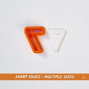 Könnte beinhalten: Zwei Plastik-Ausstecher in Form der Zahl Sieben. Der Ausstecher links ist orange und der Ausstecher rechts ist weiß. Der Text "SHARP EDGES • MULTIPLE SIZES" ist in weiß auf orangefarbenem Hintergrund am unteren Rand des Bildes gedruckt.