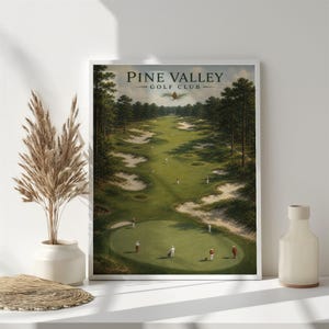 May include: A framed print of a golf course, with the text "PINE VALLEY GOLF CLUB" at the top. The artwork shows a green golf course with players, surrounded by trees and sand traps. The print is displayed on a white wall.