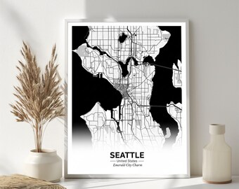 May include: A framed black and white map print of Seattle, Washington, with the city name and "Emerald City Charm" text. The map shows streets and waterways. The print is displayed on a white surface.