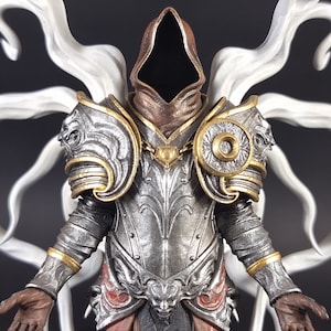 Peut inclure: Une figurine d&eacute;taill&eacute;e d'une figure capuchonn&eacute;e portant une armure argent&eacute;e et dor&eacute;e avec une aura blanche et fum&eacute;e. La figure a une capuche brun fonc&eacute; et une cuirasse argent&eacute;e avec des d&eacute;tails complexes.