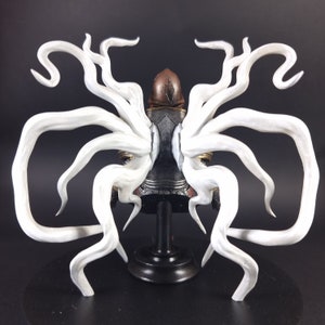Peut inclure: Une figurine blanche en forme de tentacule avec une figurine sombre et d&eacute;taill&eacute;e au centre. La figurine est pos&eacute;e sur une base noire.