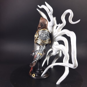 Peut inclure: Une figurine peinte en argent et or repr&eacute;sentant un chevalier avec une aile blanche sculpt&eacute;e en forme de tentacule. Le chevalier porte un casque avec un masque facial et une cape rouge et or.