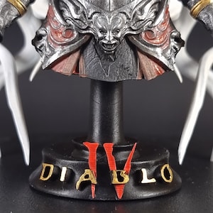 Peut inclure: Une figurine Diablo IV noire et rouge avec des lettres dor&eacute;es sur une base noire.