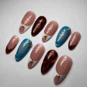 May include: Set of ten false nails with a variety of designs. Some nails are brown with a tortoiseshell pattern, some are light blue with a white tip, and some are nude with a white tip and a gold star accent.