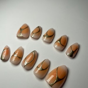 May include: Set of ten peach-colored false nails with gold abstract designs.