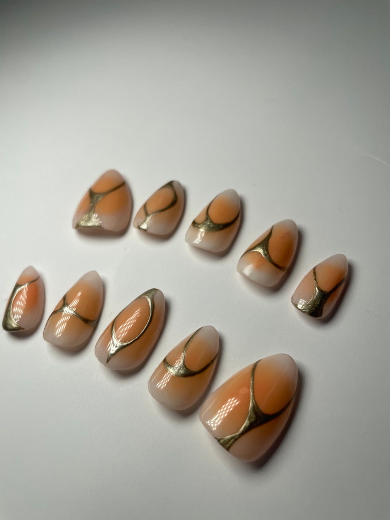 May include: Set of ten peach-colored false nails with gold abstract designs.