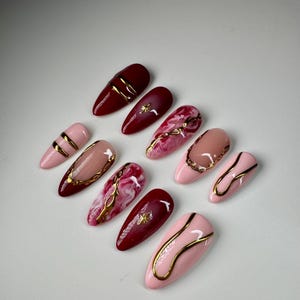 May include: Set of ten false nails with a burgundy and pink base and gold accents. Some nails have a marble design with gold veins.