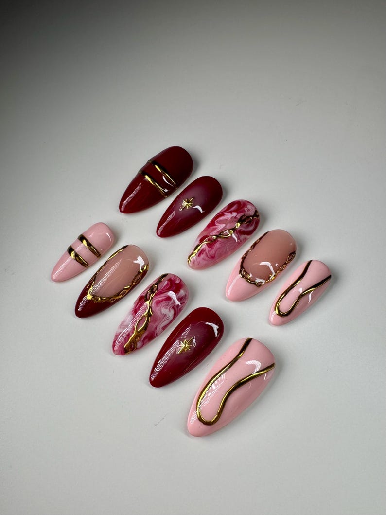 May include: Set of ten false nails with a burgundy and pink base and gold accents. Some nails have a marble design with gold veins.