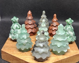 May include: A set of eight hand-carved stone Christmas tree ornaments in shades of green, brown, and gray. The ornaments are arranged on a hexagonal wooden base.