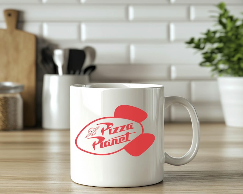 May include: White ceramic mug with a red Pizza Planet logo. The logo features the words "Pizza Planet" in a stylized font, with a planet and rocket ship design. The mug has a curved handle and is set on a wooden surface.