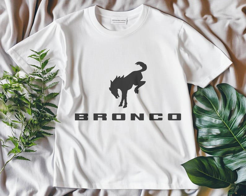 May include: White t-shirt with a black silhouette of a rearing horse and the word "BRONCO" printed on the front.