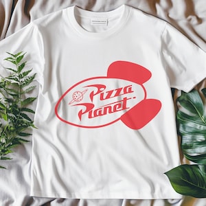 May include: White t-shirt with a red Pizza Planet logo. The logo features a stylized planet with a ring and the words "Pizza Planet" in a retro font. The shirt is made of a soft material and has short sleeves.