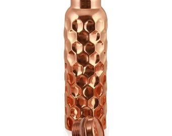 Könnte beinhalten: Eine Kupfer-Wasserflasche mit Wabenmuster und Schraubverschluss. Die Flasche hat eine glänzende, metallische Farbe und ist für Flüssigkeiten bestimmt. Der Deckel liegt neben der Flasche.