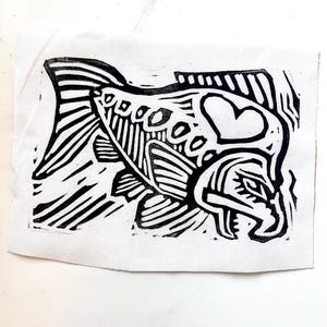 May include: Black and white linocut print of a stylized fish with a heart on its head.