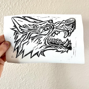 May include: Black and white linocut print of a wolf's head with its mouth open and teeth showing.