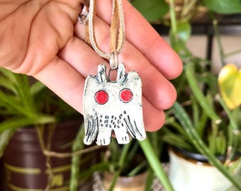 May include: A silver owl pendant with red eyes on a brown leather cord necklace.
