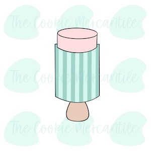 May include: A cookie cutter in the shape of a popsicle. The top is a light pink cylinder, the middle is a light blue rectangle with vertical stripes, and the bottom is a light brown shape. The Cookie Mercantile logo is in the background.