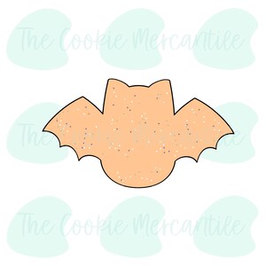 Puede incluir: Un cortador de galletas con forma de murciélago con un diseño naranja moteado. El cortador está delineado en negro.
