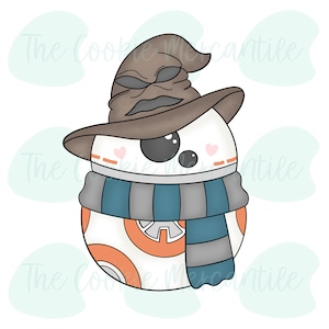Op de afbeelding: Een witte en oranje BB-8 droid koekjesvormer met een bruine tovenaarshoed en een blauw-grijze gestreepte sjaal.