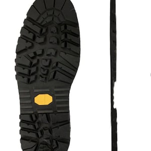 May include: Close-up view of the bottom of a black leather boot with a yellow rubber tread. The boot sole is designed for traction and grip.