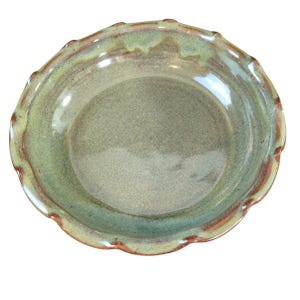 May include: A round ceramic pie dish with a scalloped edge, featuring a glossy glaze in shades of sage green and olive, with warm brown tones along the fluted rim and a smooth, slightly concave center surface for baking various food items.