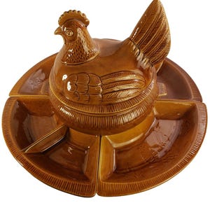 May include: A brown ceramic serving dish in the shape of a hen. The hen sits atop a divided serving platter with four sections. The dish has a glossy finish and is designed for serving snacks or appetizers.