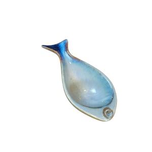 May include: A ceramic fish-shaped dish with a light blue interior and a dark blue tail. The dish has a small, round eye detail and a gold-colored rim. The overall design is smooth and glossy, suitable for serving small portions.