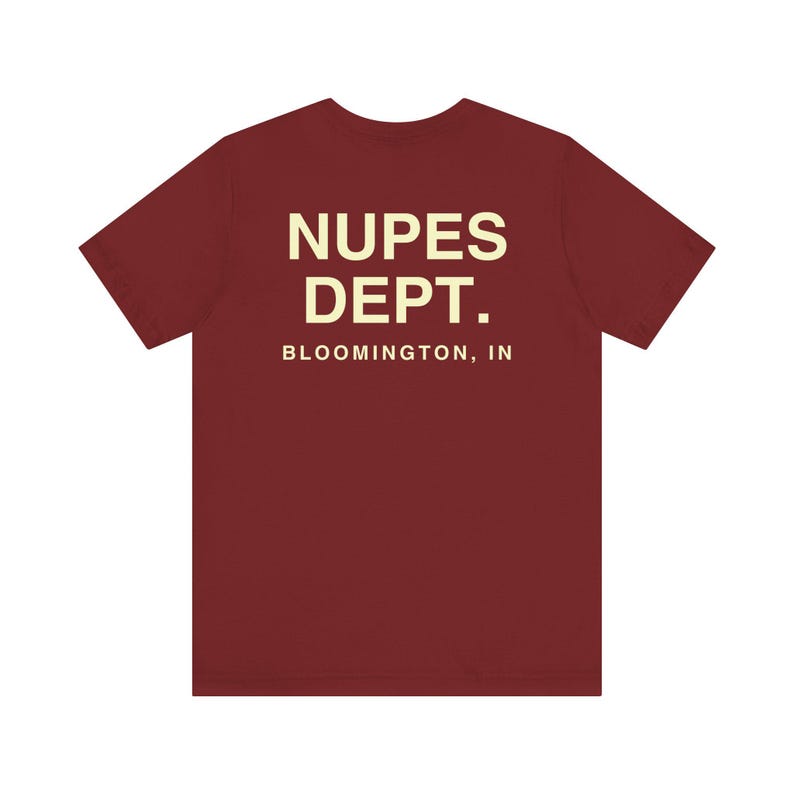 May include: A maroon t-shirt with the text "NUPES DEPT. BLOOMINGTON, IN" printed in a cream color. The shirt has short sleeves and a crew neck.