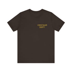 May include: A dark brown t-shirt with the text "CENTAUR DEPT." printed in gold on the upper chest area. The shirt has short sleeves and a crew neck.