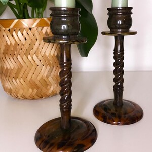 May include: Two brown and black tortoiseshell candle holders with a twisted design and a green candle in each.