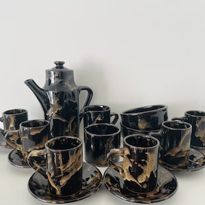 May include: A black and gold ceramic coffee set with a teapot, cups, saucers, and a bowl. The set has a marbled design with black and gold swirls.