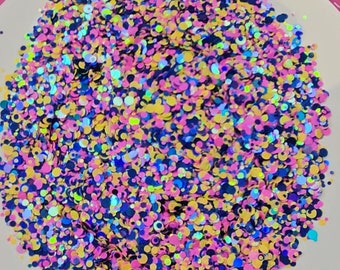 May include: A close-up of a white plate filled with colorful iridescent glitter. The glitter is in various sizes and shapes, including circles, squares, and stars. The glitter is arranged in a random pattern, creating a visually appealing and sparkly effect.