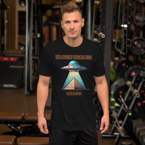 May include: Black t-shirt with a graphic of a UFO hovering over a pyramid. The text "THE ANCIENT ENIGMA FILES" is above the UFO and "ENIGMACAST" is below the pyramid.