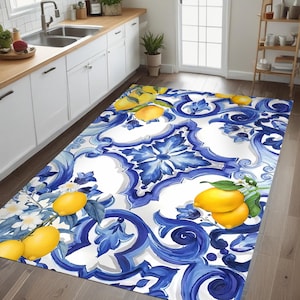 Op de afbeelding: Een rechthoekig keukenkleed met een witte achtergrond en een blauw-wit bloemmotief. Het kleed heeft gele citroenen en groene bladeren. Het kleed ligt op een houten vloer voor een witte keuken.