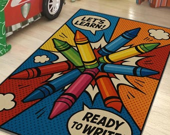 May include: A rectangular rug with a colorful crayon design. The rug features a blue background with a pop art style design of crayons in various colors, including red, orange, yellow, green, and blue. Text bubbles read "LET'S LEARN!" and "READY TO WRITE!"