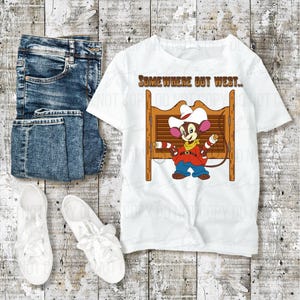 Peut inclure: T-shirt blanc avec une souris de dessin animé portant un chapeau de cow-boy et le texte "SOMEWHERE OUT WEST..". Le t-shirt est associé à un jean bleu et des baskets blanches, sur un fond en bois.