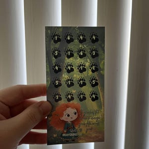 May include: A rectangular card featuring a cartoon illustration of a character with red hair and a green dress. The card has black paw prints with numbers on a forest background. Text on the card reads "If you have the heart to change, your fate will surely change".