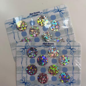 May include: Two sheets of stickers with holographic, circular designs. Each sheet has a blue and white plaid pattern with blue bows. The text "Low Income" and "High Income" are visible on the sheets.